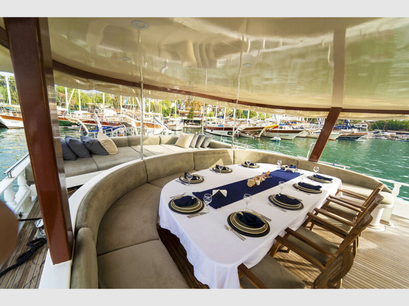 Diamond Lila charter gulet outdoor wide angle shot of aft deck featuring dining table and sunbeds
